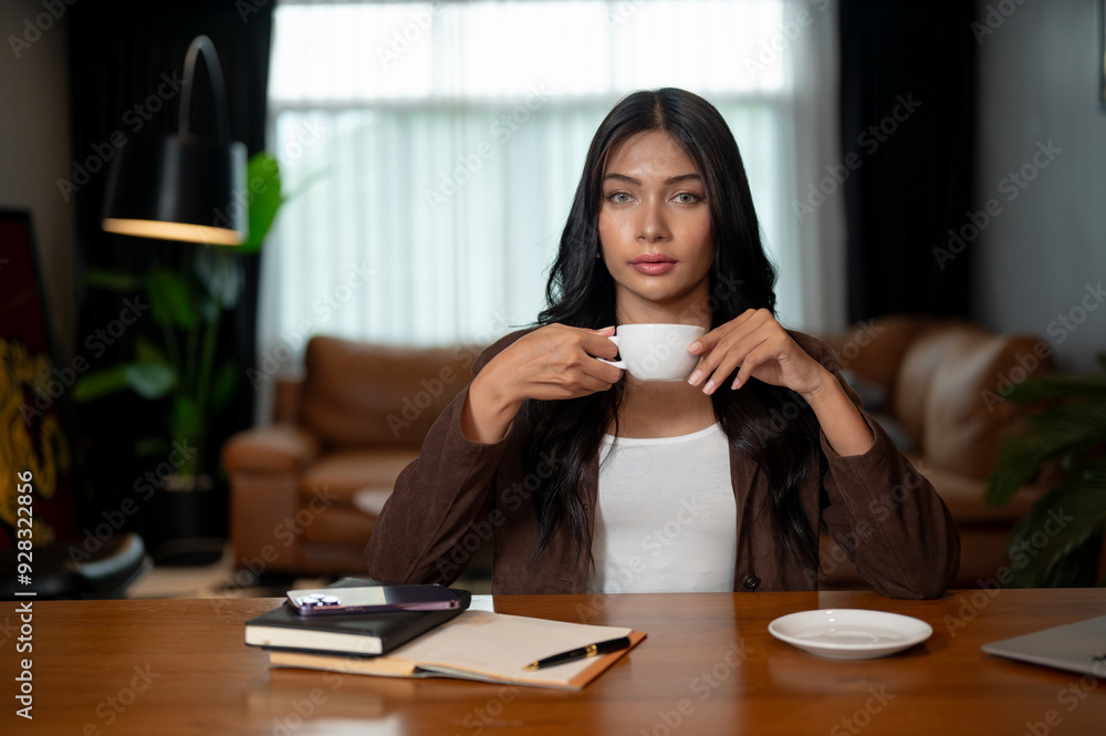 A businesswoman is sitting at her desk with a coffee cup in her hand, looking at the camera.