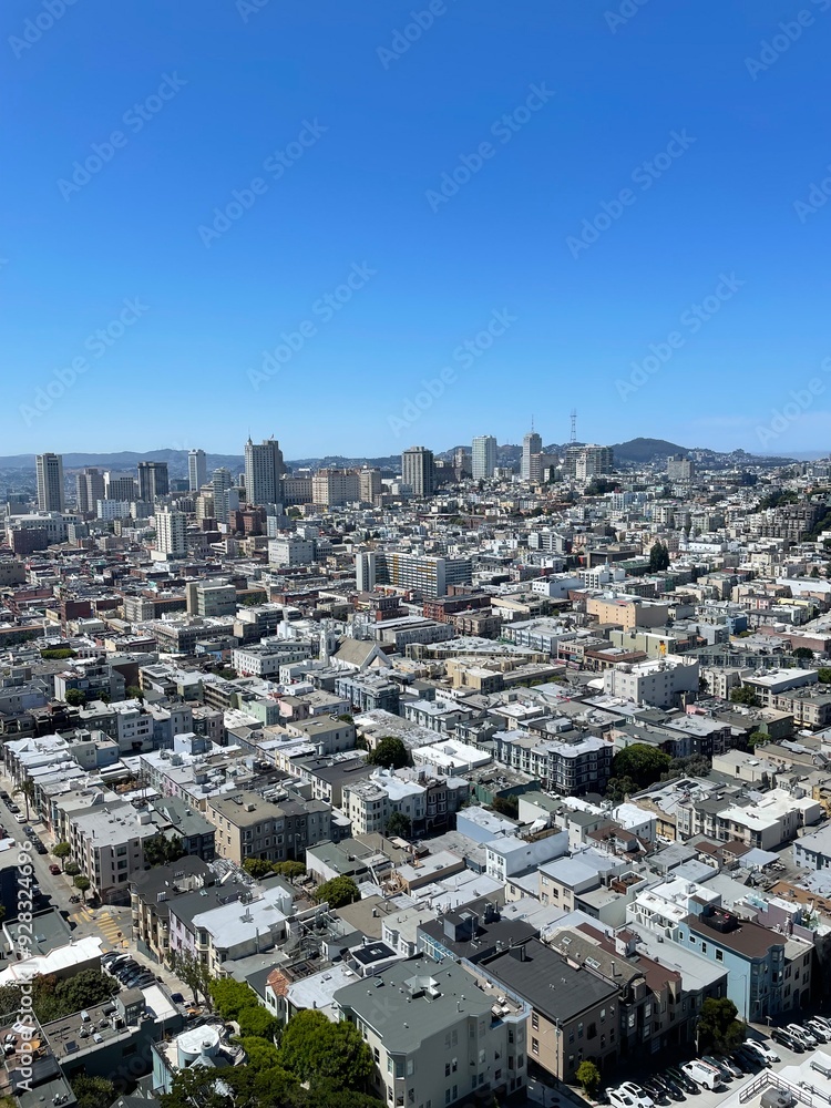 Fototapeta premium San Francisco von oben. Strahlend blauer Himmel, hinten stehen Hochhäuser vor Hügeln. Zahlreiche Häuser.