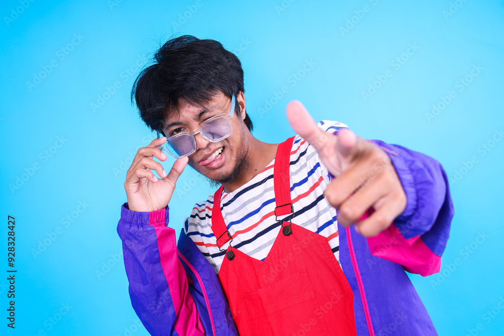 Young Asian Man Feeling Vibrant and Energetic in Colorful Clothes Pointing To Camera Against Blue Background Young Asian Man Feeling Vibrant and Energetic in Colorful Clothes Pointing To Camera Against Blue Background