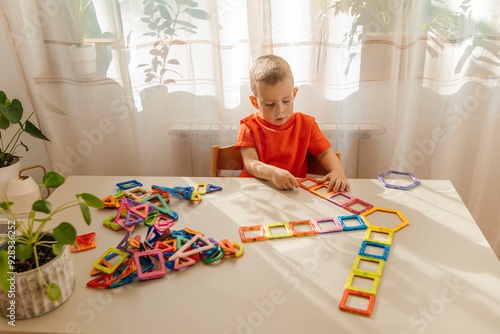 Boy arranging magnetic toy blocks on table at home photo