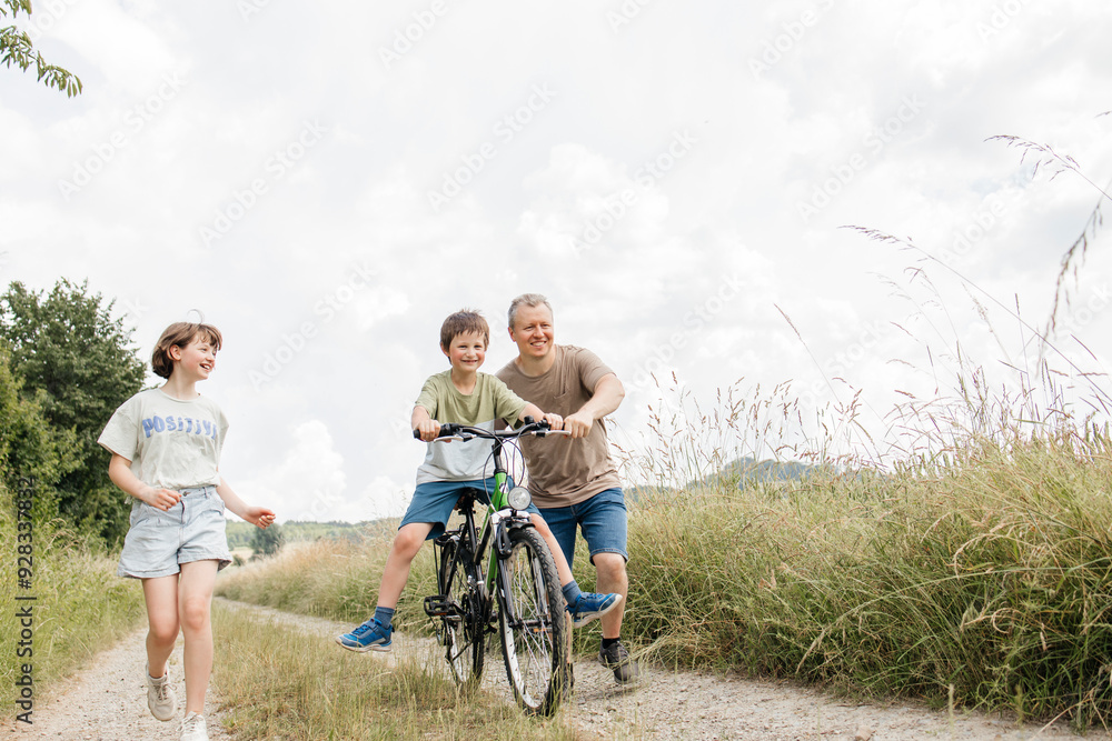 Father and daughter enjoying with boy riding bicycle on field Father and daughter enjoying with boy riding bicycle on field