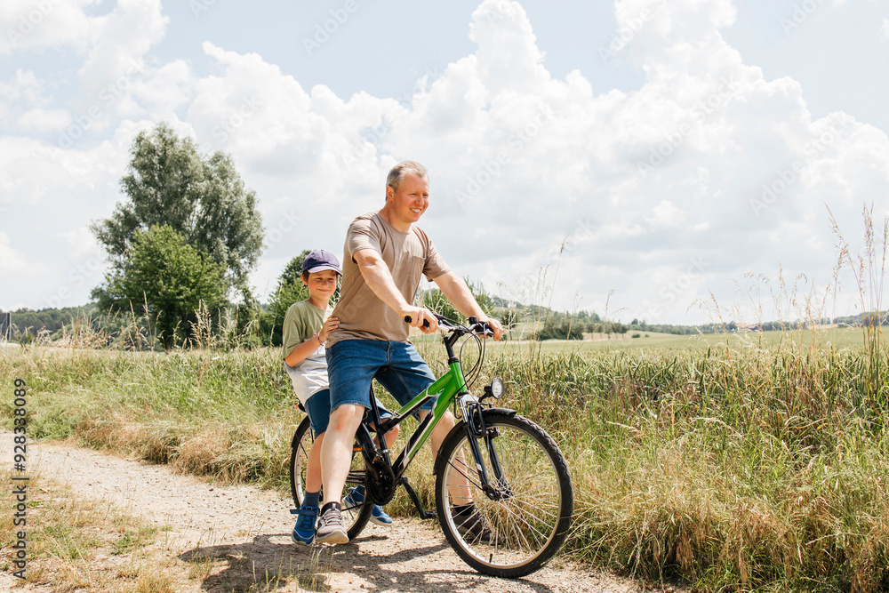 Son sitting behind father on bicycle near field Son sitting behind father on bicycle near field