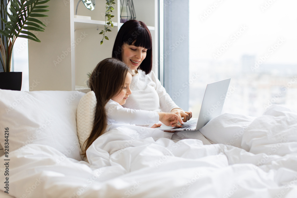 Mother and daughter lying in bed using laptop. Cozy family bonding moment, shared technology experience, modern parenting, relaxed indoor setting. Mother and daughter lying in bed using laptop. Cozy family bonding moment, shared technology experience, modern parenting, relaxed indoor setting.