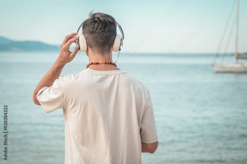 young man on beach with back turned wearing headphones young man on beach with back turned wearing headphones