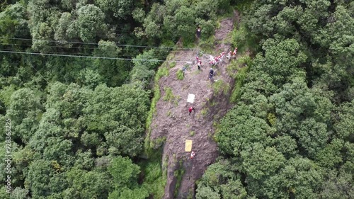 A group of children, guided by their coach, rappel down a forested cliff during a summer camp adventure. photo