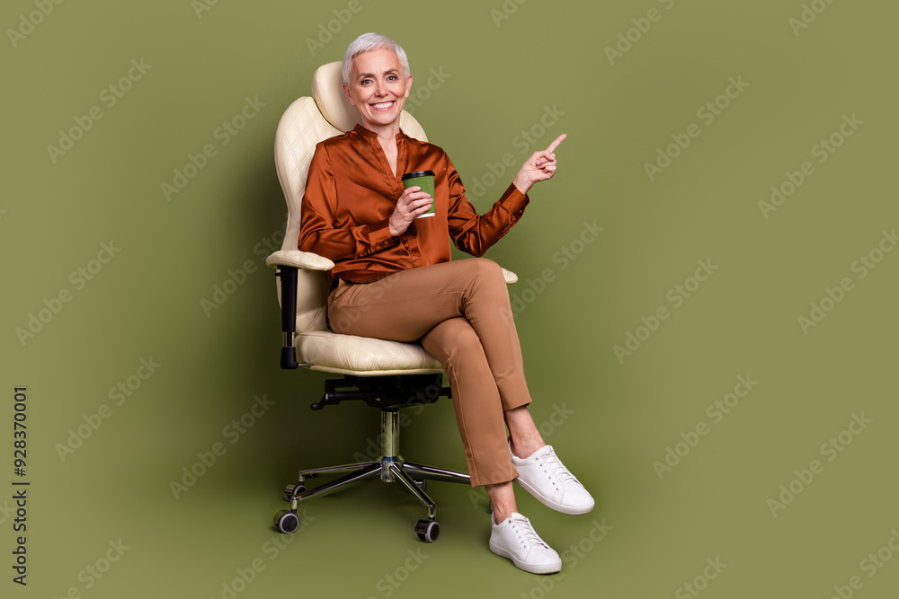 Fototapeta premium Full body photo of senior woman sit office armchair coffee point empty space dressed brown formalwear isolated on khaki color background