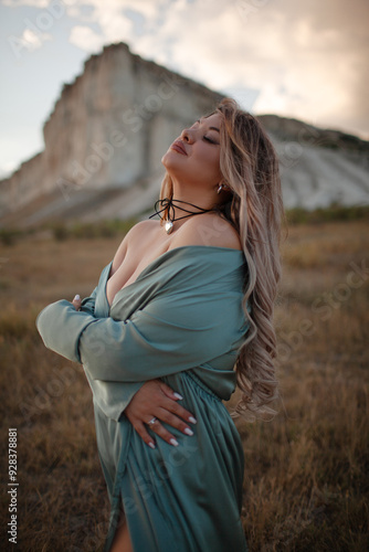 A woman plus size dressed in a dress walking against the background of a white mountain. Beautiful girl with a long hair developing in the wind travels