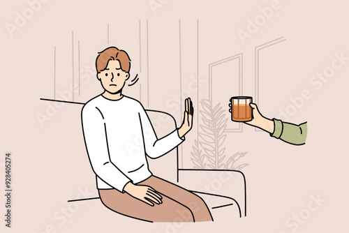 Determined man refuses alcohol, demonstrates stop gesture, sitting on sofa near hand with whiskey. Guy says no to alcohol and wants to live sober lifestyle to avoid hangover and intoxication