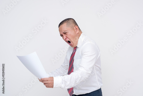 A middle aged asian manager screaming in frustration after reading disappointing figures on a piece of paper. Scratching his head in exasperation. Isolated on a white background. photo