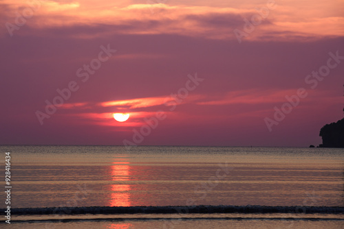 Sunset at Pak Meng Beach in Trang , Fiery red sun dips below the horizon, painting the beach in warm hues of orange, pink, and purple. Gentle waves lap at the shore 