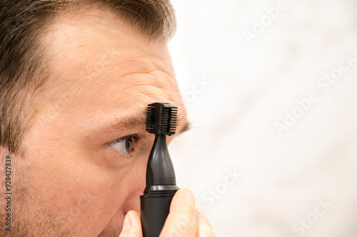 A man is trimming his eyebrows with a razor. Self-care. Morning routine. Close-up of the face photo