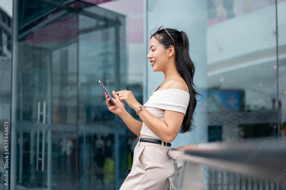 An elegant Asian woman is chatting on her smartphone while standing in front of the building. An elegant Asian woman is chatting on her smartphone while standing in front of the building.