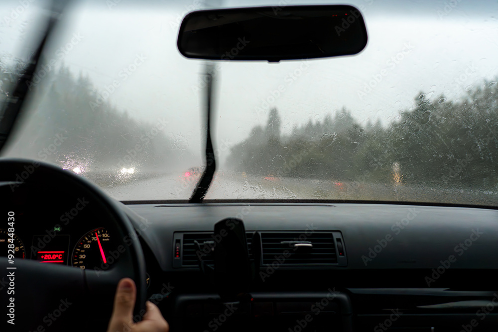 Obraz premium A car is driving along the road during the rain and the windshield wipers are wiping the windshield of the car.