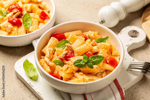 Plates with Chicken tomato pasta, decoarated with basil on a beige table background. photo