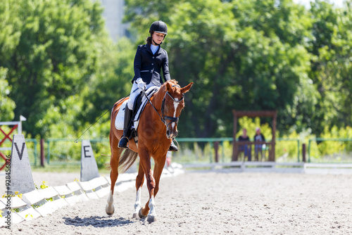 Equestrian rider competes in dressage test on a sunny day at an outdoor arena