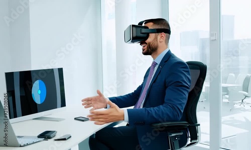 Businessman Experiencing VR: A young,  bearded businessman wearing a VR headset,  engrossed in a digital experience,  sits at his desk in a modern office with a computer screen showing a blue data cha