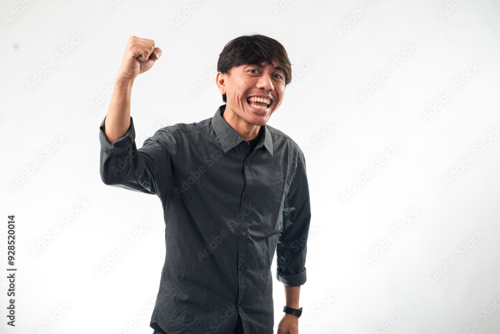 A smiling Asian man in a dark grey button-up shirt makes a triumphant gesture with raised fists and an enthusiastic expression against a plain white background, perfect for motivational A smiling Asian man in a dark grey button-up shirt makes a triumphant gesture with raised fists and an enthusiastic expression against a plain white background, perfect for motivational