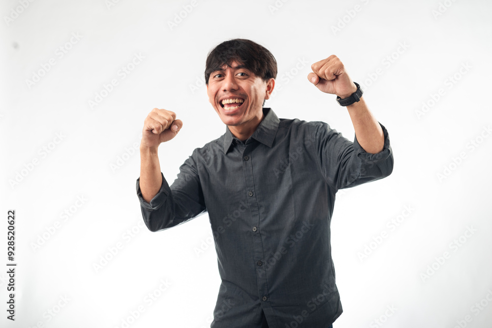 A smiling Asian man in a dark grey button-up shirt makes a triumphant gesture with raised fists and an enthusiastic expression against a plain white background, perfect for motivational A smiling Asian man in a dark grey button-up shirt makes a triumphant gesture with raised fists and an enthusiastic expression against a plain white background, perfect for motivational