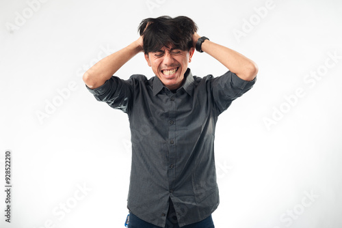 An Asian man in a dark gray shirt is grabbing his hair with both hands, showing visible frustration and stress on his face against a plain white background.