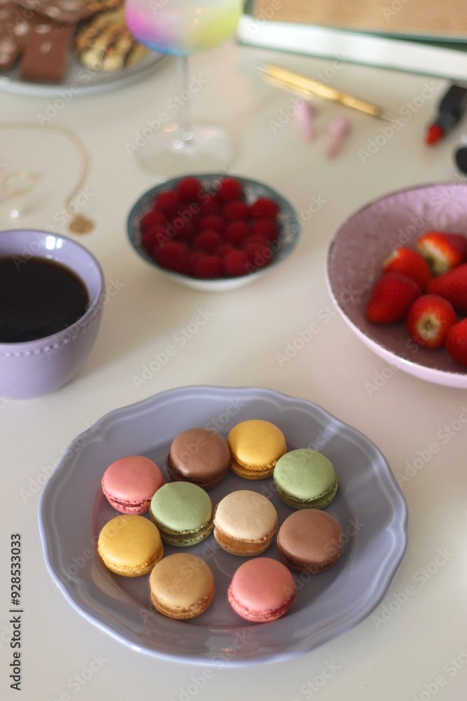 Plate of pastel macarons, cookies and chocolate, cup of tea of coffee, glass of bubble water, various berries, books and accessories on the table. Selective focus, pastel colors. Plate of pastel macarons, cookies and chocolate, cup of tea of coffee, glass of bubble water, various berries, books and accessories on the table. Selective focus, pastel colors.