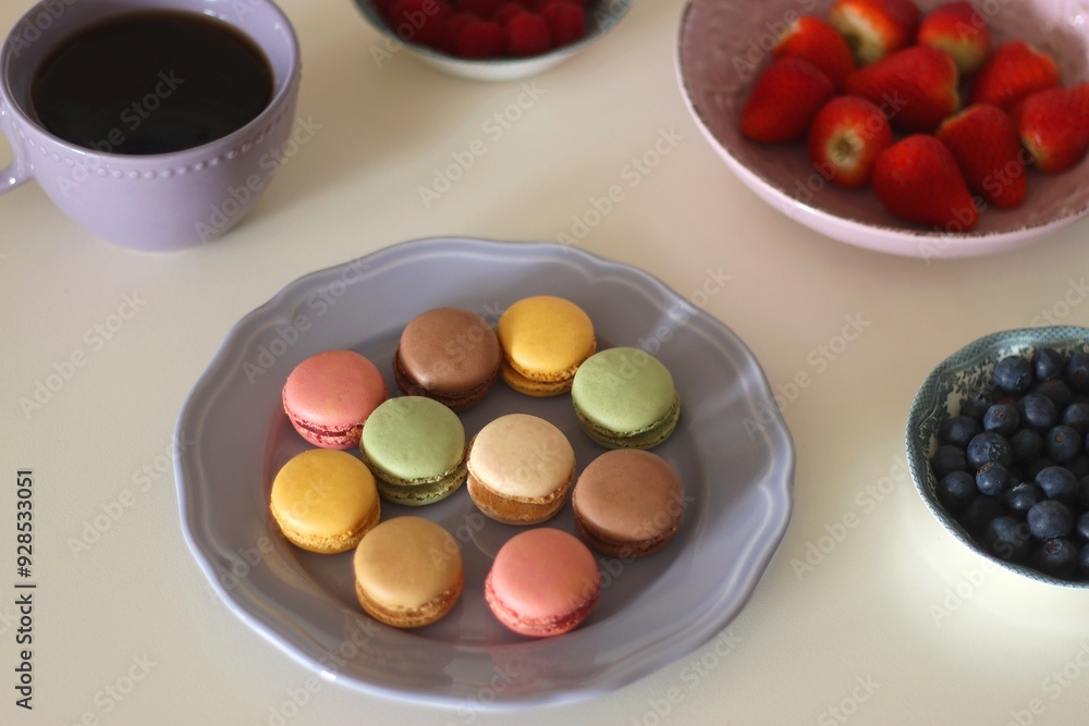 Plate of pastel macarons, cookies and chocolate, cup of tea of coffee, glass of bubble water, various berries, books and accessories on the table. Selective focus, pastel colors. Plate of pastel macarons, cookies and chocolate, cup of tea of coffee, glass of bubble water, various berries, books and accessories on the table. Selective focus, pastel colors.