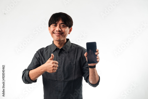 An Asian man in a gray shirt, smiling while holding a smartphone in one hand and giving a thumbs-up with the other. The plain background emphasizes his positive gesture and approval.