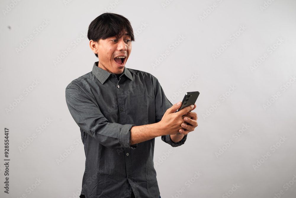 A smiling Asian man in a dark gray shirt interacts with a smartphone, looking down as he types with both hands. The casual and friendly atmosphere suggests he is engaged in a pleasant conversation A smiling Asian man in a dark gray shirt interacts with a smartphone, looking down as he types with both hands. The casual and friendly atmosphere suggests he is engaged in a pleasant conversation