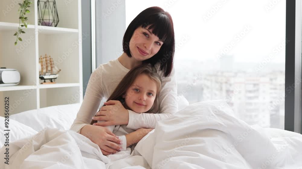 Mother and daughter hugging in bed in bright, cozy bedroom. They look content and happy, sharing a moment of love and comfort. Bonding between parent and child in a serene, peaceful setting. Mother and daughter hugging in bed in bright, cozy bedroom. They look content and happy, sharing a moment of love and comfort. Bonding between parent and child in a serene, peaceful setting.