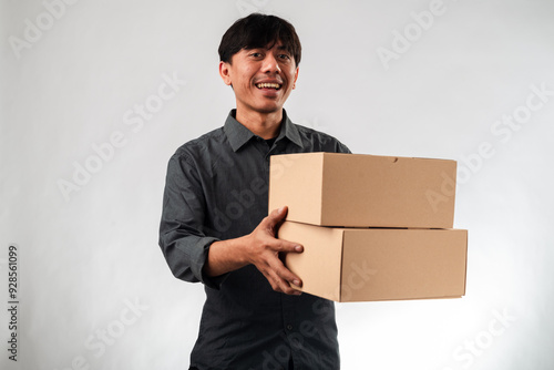 Asian man in a dark gray shirt holding out a plain cardboard box with both hands, standing against a white background. The box is central to the image, suggesting delivery, packaging, or a gift.