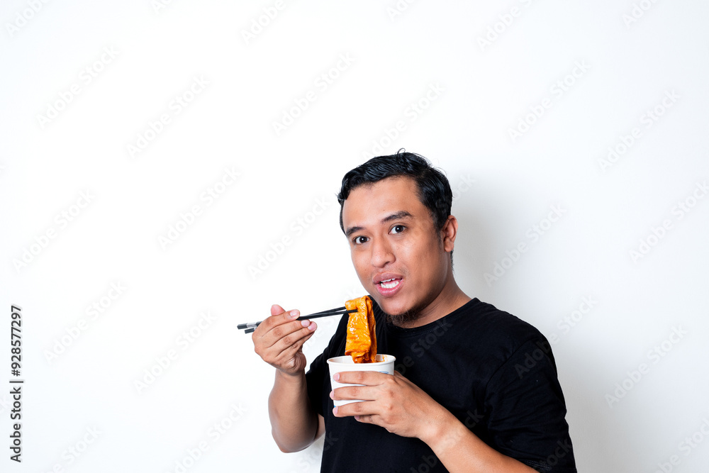 Asian adult man wearing a black t-shirt posing eating Korean specialty food odeng isolated white background Asian adult man wearing a black t-shirt posing eating Korean specialty food odeng isolated white background