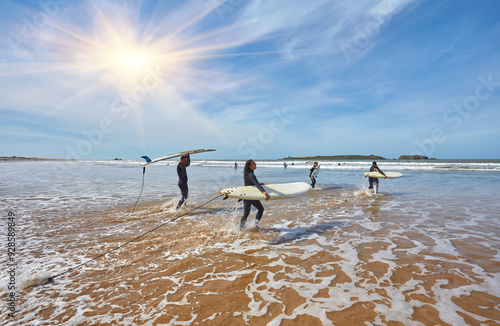 Photography A pack of young surfers dashes into the ocean, boards in hand, eager to greet the oncoming waves