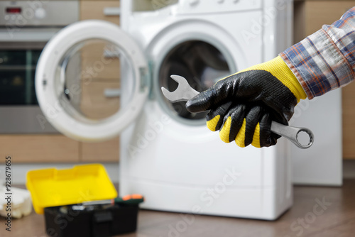 Close-up a hand a household appliance repairman with wrench against the backdrop of a domestic washing machine.