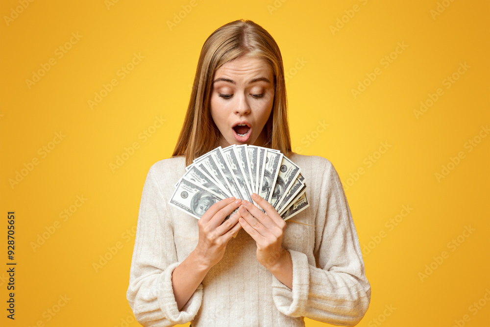 Big win. Shocked young girl holding fan of dollar banknotes, orange background with free space Big win. Shocked young girl holding fan of dollar banknotes, orange background with free space