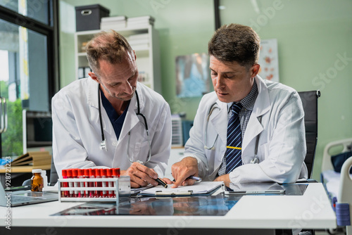 Caucasian middle-aged male doctor and Italian scientific researcher are seated at desk, discussing innovative antiviral drug inventions, with a monitor displaying the latest technology advancements.