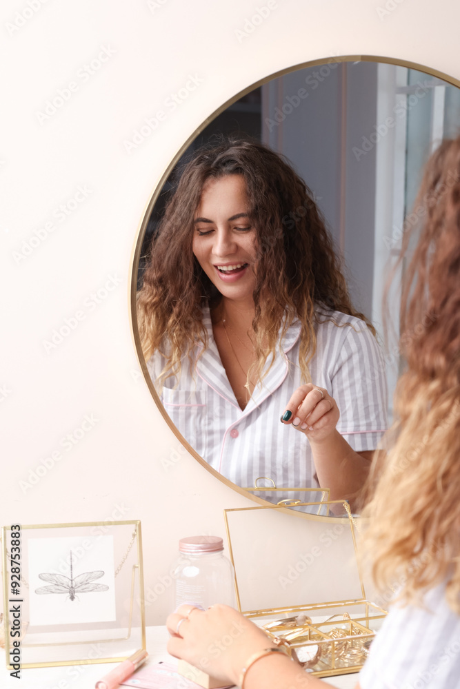 A beautiful curly-haired girl in striped pajamas preens herself in front of the mirror. A woman makes up in the morning, chooses jewelry. A woman looks in the mirror in her bedroom, smile A beautiful curly-haired girl in striped pajamas preens herself in front of the mirror. A woman makes up in the morning, chooses jewelry. A woman looks in the mirror in her bedroom, smile