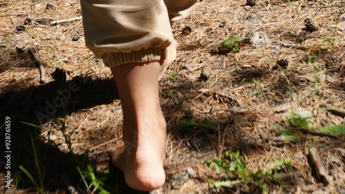 A woman walks barefoot along forest path, feeling soft earth beneath her feet. Tranquility of forest surrounds her as she enjoys beauty of nature. Forest path offers walk into lush forest landscape.