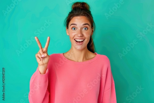 A joyful young woman with freckles playfully posing against a vibrant turquoise background while enjoying a moment of happiness