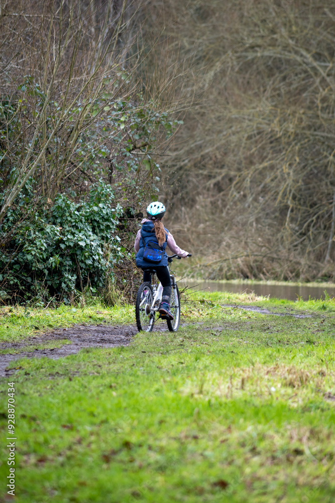 Naklejka premium Rear View of a Young Girl Cycling through a Forest Path in Early Spring
