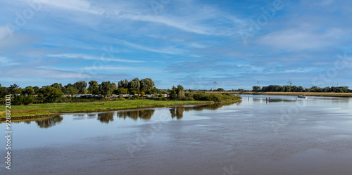 Landschaftsbild der Ems und seiner Uferzone. Friedlich fließt die Ems dahin , vorbei an dem  grünen Land der Uferzone. Der Himmel erscheint mit schönen , leichten Zeichnungen in sommerlichem blau photo