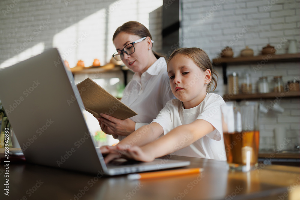 Girl using laptop while mother reading book at home Girl using laptop while mother reading book at home
