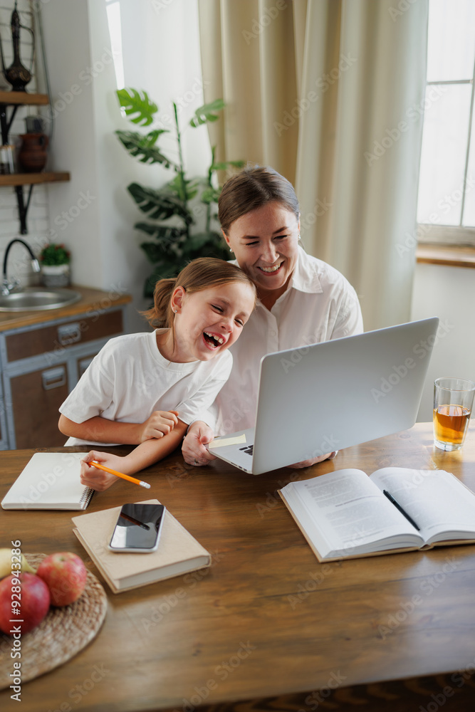 Smiling mother and daughter using laptop near books in kitchen Smiling mother and daughter using laptop near books in kitchen