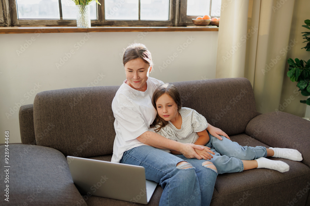 Mother and girl looking at laptop while resting on couch at home Mother and girl looking at laptop while resting on couch at home