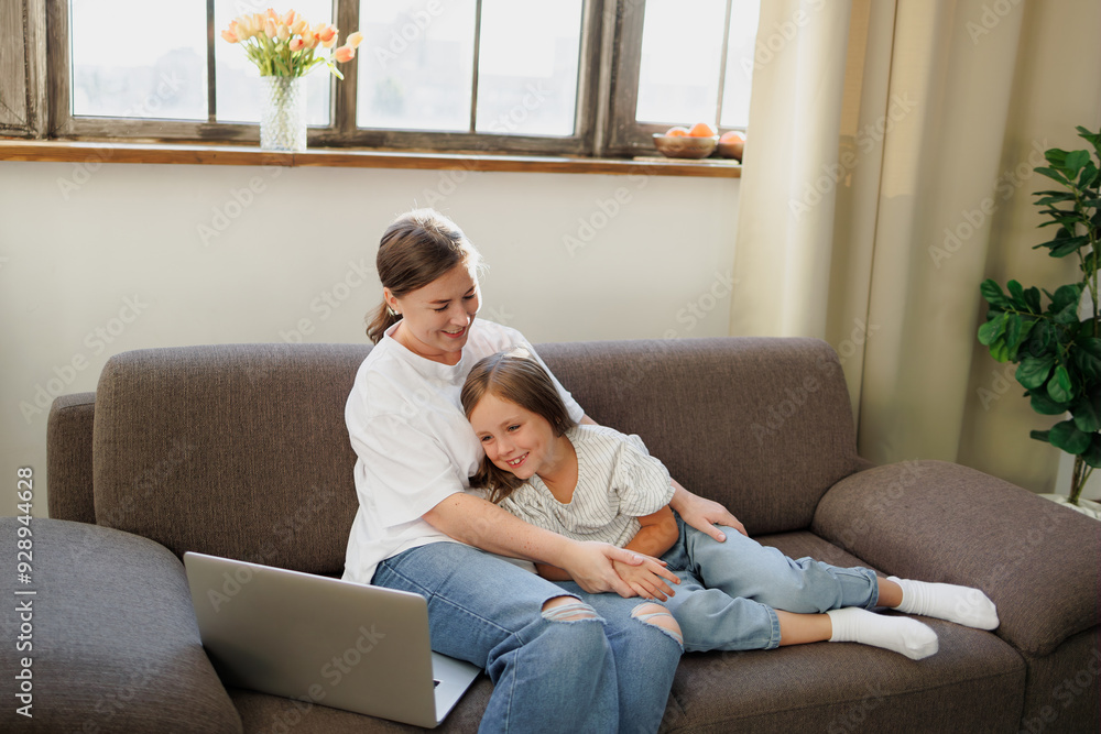 Smiling mother hugging daughter near laptop at home Smiling mother hugging daughter near laptop at home