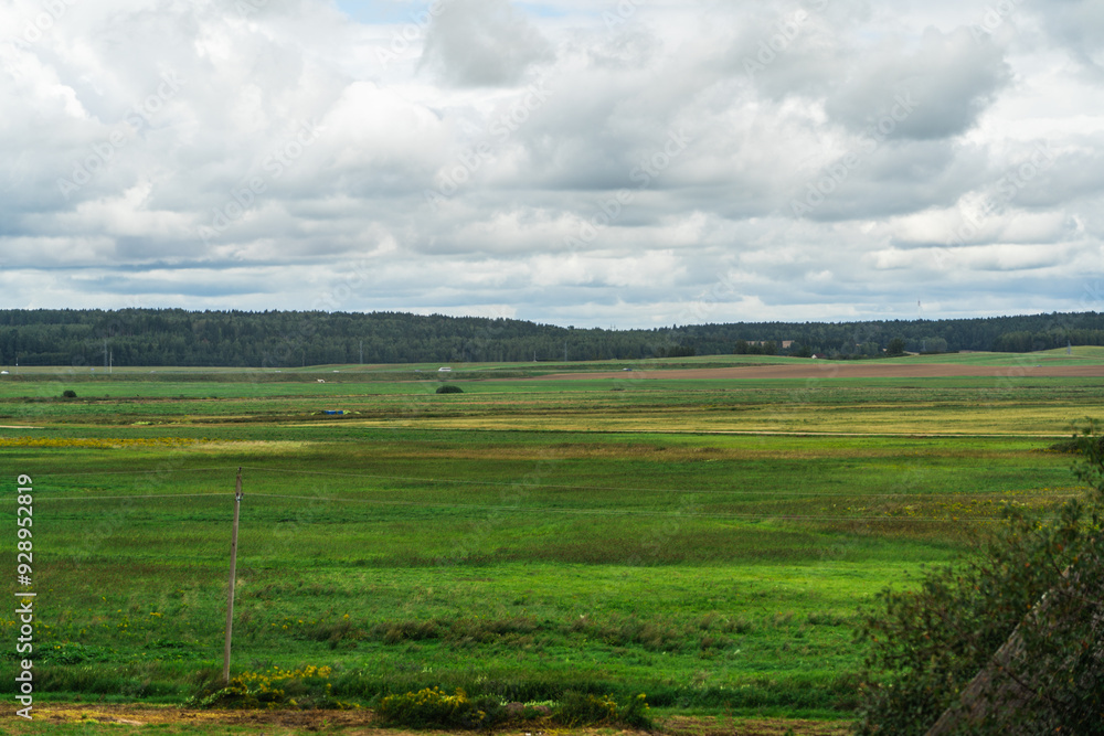 Green fields in the village. Cloudy sky over the fields. Highway in the distance Green fields in the village. Cloudy sky over the fields. Highway in the distance