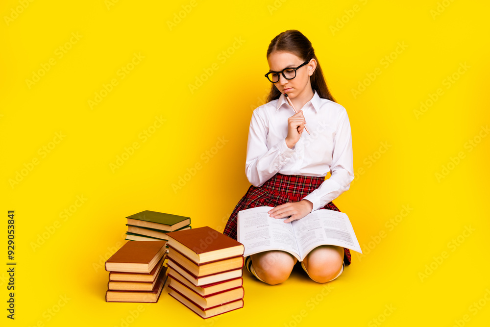 Full size photo of charming teen pupil girl sit floor books pile minded look wear trendy uniform isolated on yellow color background Full size photo of charming teen pupil girl sit floor books pile minded look wear trendy uniform isolated on yellow color background