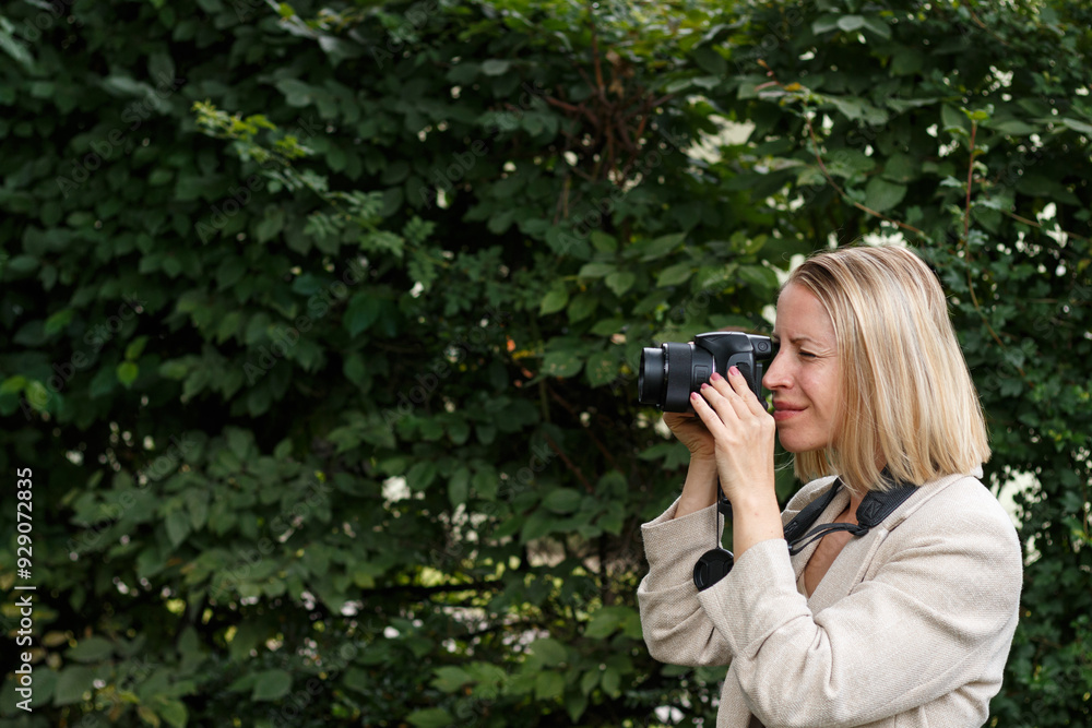 Young blonde woman taking a photo in front of green bushes. Young blonde woman taking a photo in front of green bushes.
