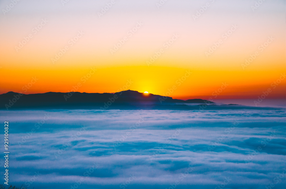 Obraz premium Golden sun rising behind mountains, illuminating a dreamy sea of clouds