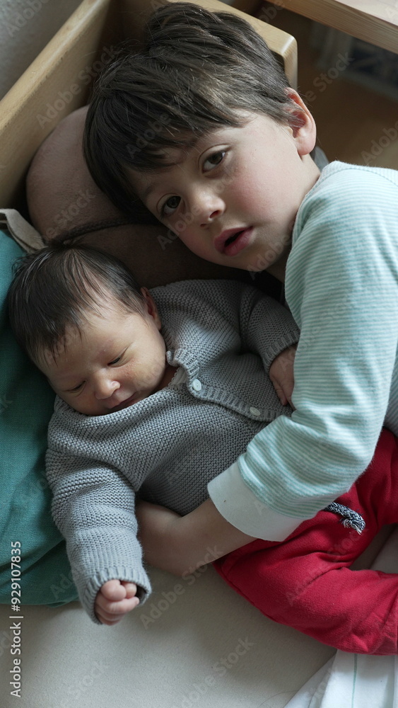 Older brother lovingly cuddles his newborn sibling, both lying comfortably on a bed, showcasing a tender moment of sibling bond and affection Older brother lovingly cuddles his newborn sibling, both lying comfortably on a bed, showcasing a tender moment of sibling bond and affection