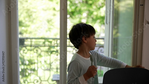 Young boy reaching for the window knob, stepping out onto the balcony to explore, and returning home to close the window. curiosity and interaction with the outdoor environment