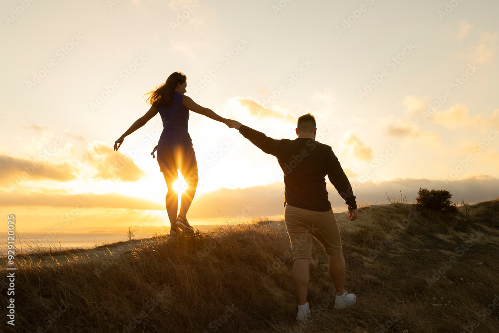 Fototapeta premium Loving couple walking on a hill at sunset holding hands